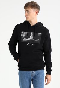 Black hoodie made of cotton blend, featuring a graphic design of hands in prayer and text below. Kangaroo pocket at the front.