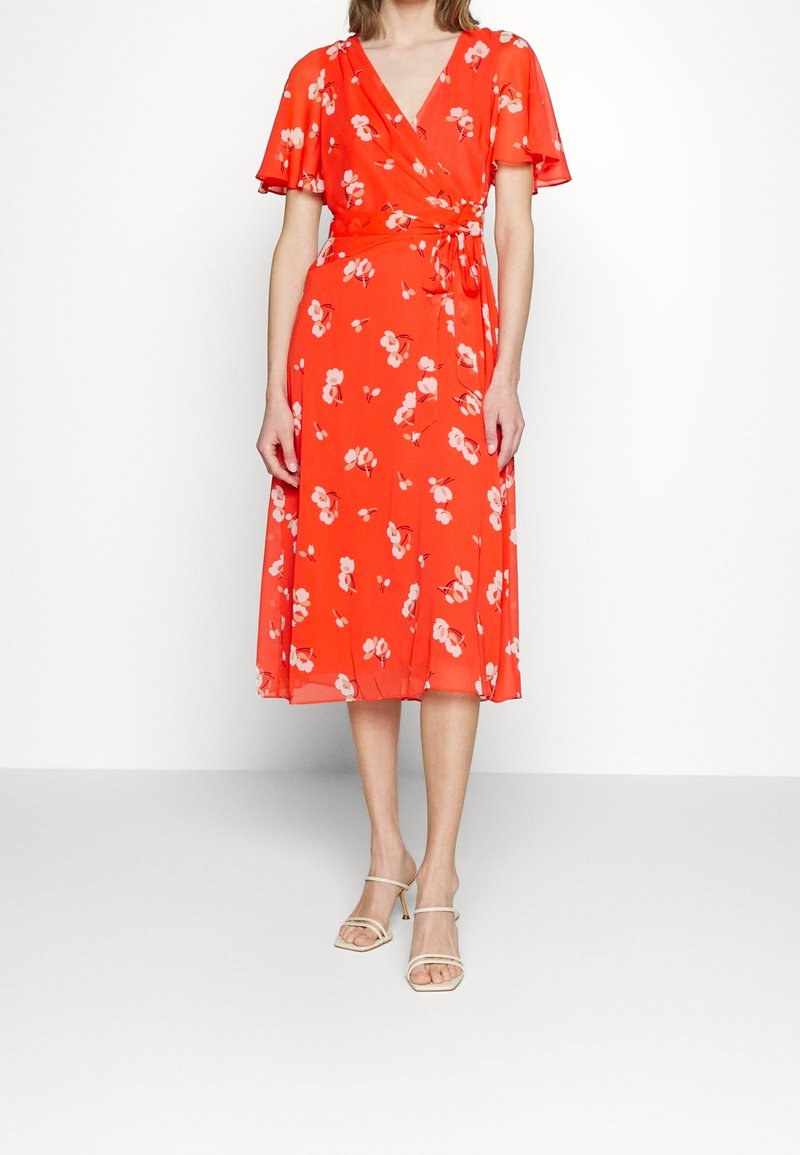 Robe portefeuille rouge à fleurs avec des manches courtes volantées, un décolleté en V et une taille nouée. Le tissu est léger et semi-transparent.