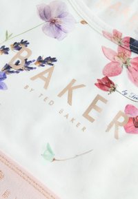 Hvid kortærmet skjorte med blomsterprint i lilla og pink. "BAKER" i rosaguld bogstaver under designet. Blødt stof.