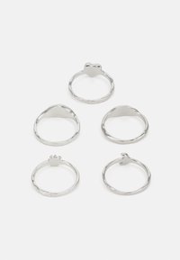 Conjunto de cinco anillos de metal plateado con diversos diseños, incluyendo una forma de corazón, bandas lisas y texturizadas, y un acento de gema.