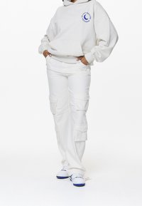 Sudadera blanca con un gráfico azul de "No Molestar", combinada con pantalones cargo blancos que tienen múltiples bolsillos y zapatillas blancas con acentos azules.