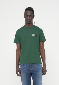 Πράσινο βαμβακερό T-shirt με κοντά μανίκια και στρογγυλή λαιμόκοψη. Διαθέτει εκτυπωμένο λογότυπο σε άσπρο και μαύρο στην αριστερή πλευρά του στήθους.