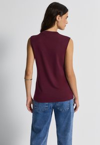 Top marón sin mangas hecho de una tela suave, con escote redondo. Combinado con pantalones de mezclilla azul claro, que presentan un ajuste relajado.
