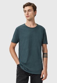 Mörk teal kortärmad t-shirt med rund halsringning, något avslappnad passform och textilstruktur. Anmärkningsvärd sömdetalj vid halslinningen.