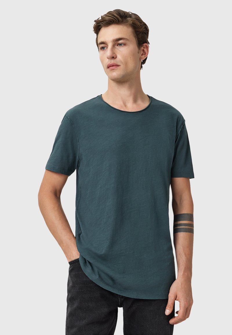 Mörk teal kortärmad t-shirt med rund halsringning, något avslappnad passform och textilstruktur. Anmärkningsvärd sömdetalj vid halslinningen.