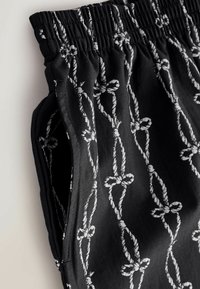 Fekete szövet rövidnadrág fehér kötélmintával, elasztikus derékrésszel és oldalzsebekkel, lágy, texturált felülettel.