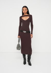 Rievots adīts kleita tumši burgundijas krāsā ar griezumu kakla izgriezumā. Kopā ar melnu jostu ar sudraba logotipa detaļu un teksturētu pelēku somu.