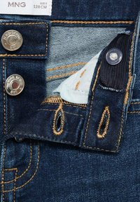 Denim-Jeansbund mit silbernen Druckknöpfen, dunklem blauen Stoff, kontrastierender oranger Naht und einer hellblauen Innen-Tasche.