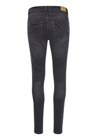 Jean en denim foncé, coupe slim, taille mi-haute, avec des poches arrière à rabat incliné et une texture légèrement délavée.