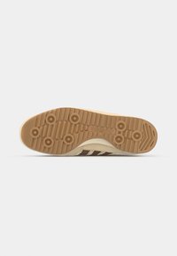 Semelle de sneaker marron et crème avec un caoutchouc texturé, des motifs de grip circulaires et des détails de logo ; elle présente une construction légère et durable.