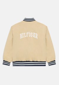 Beige bomber jacket with elastic cuffs and waistband. Features white "Hilfiger" logo across the back. Navy and white striped collar detail.