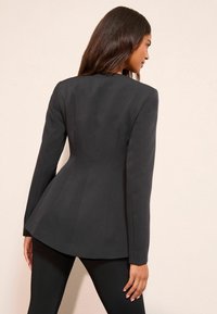 Czarna, dopasowana marynarka z długimi rękawami, dopasowaną sylwetką i baskinką u dołu. Gładka faktura tkaniny i czyste linie podkreślają projekt.