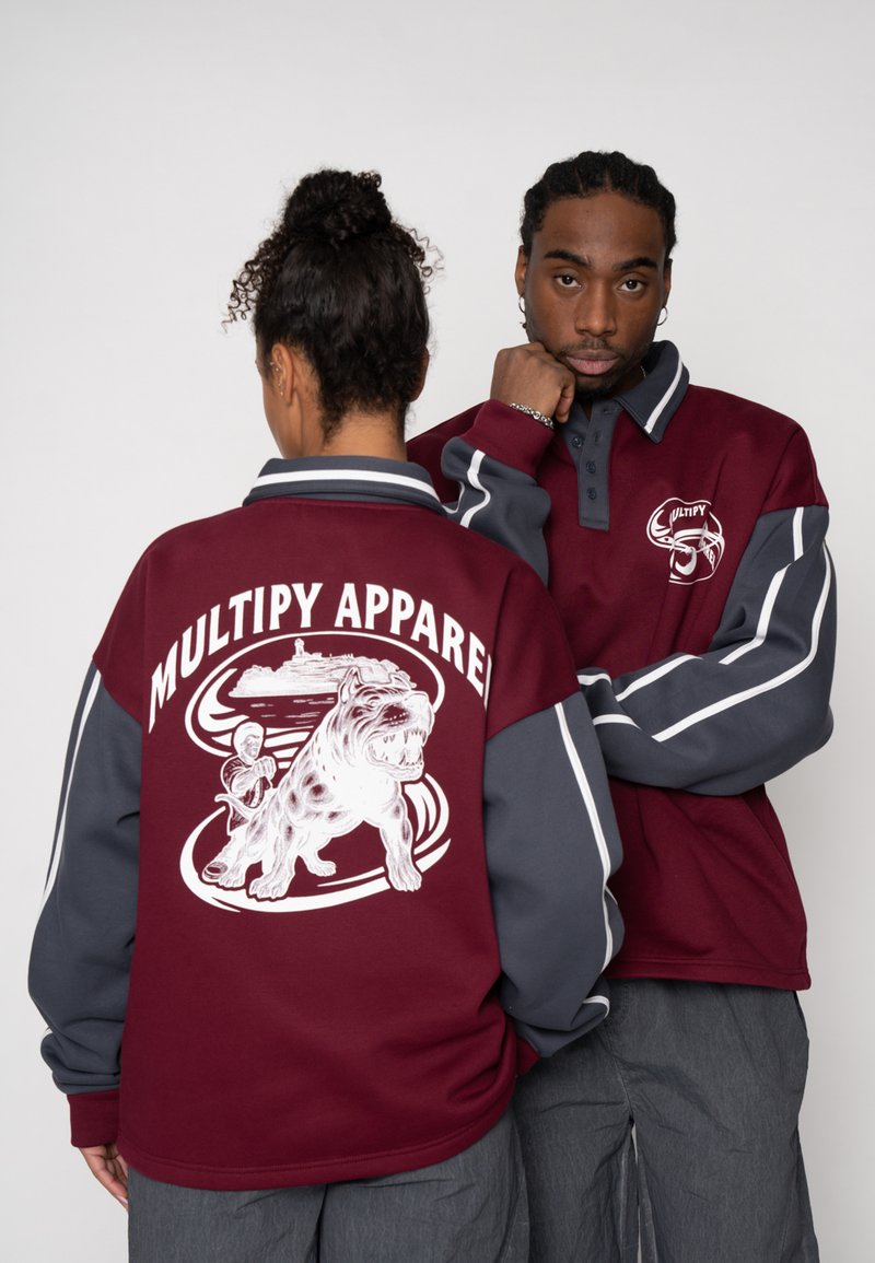 Pullover-Jacke in Kastanienbraun und Grau mit einer Hündchen-Grafik auf dem Rücken, darüber befindet sich der Schriftzug "MULTIPY APPAREL" und auf der Vorderseite ist ein gesticktes Logo zu sehen.