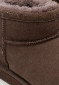 Stivaletto alla caviglia in camoscio marrone con morbida fodera interna, dettagli cuciti lungo le cuciture e apertura superiore arrotondata.