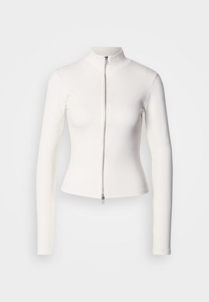 Bílý, přiléhavý top s dlouhým rukávem, vysokým límcem a předním zipem. Vyrobený z žebrované látky s hladkou strukturou a pružným střihem.