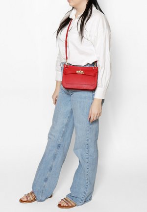 Sac bandoulière en cuir rouge avec une texture lisse, matériel doré et un design à rabat avant. Sangle ajustable et forme rectangulaire, convenant à un usage décontracté.