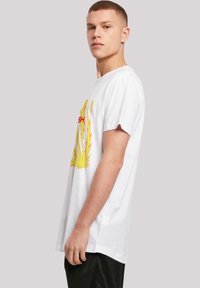 Hvid bomulds T-shirt med korte ærmer, prydet med et iøjnefaldende grafisk design i gul og rød af lyn og tekst på forsiden.