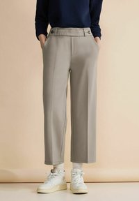 Ljusgrå vida byxor med slät front, fickor och veck fram, tillsammans med vita högskaftade sneakers och en marinblå topp.