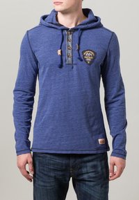 Camicia a maniche lunghe blu con cappuccio, dotata di pattina con bottoni, tessuto testurizzato, toppa sul petto e etichetta tessuta sull'orlo.