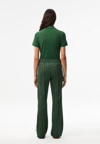 Grønn polo skjorte parret med mønstrede grønne utsvingte bukser med geometrisk design, laget av mykt stoff, med elastisk midje.