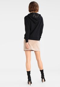 Sudadera negra con forro texturizado en la capucha, combinada con una falda mini de ante beige y botas de tacón negro. Cordon ajustable en el cuello.