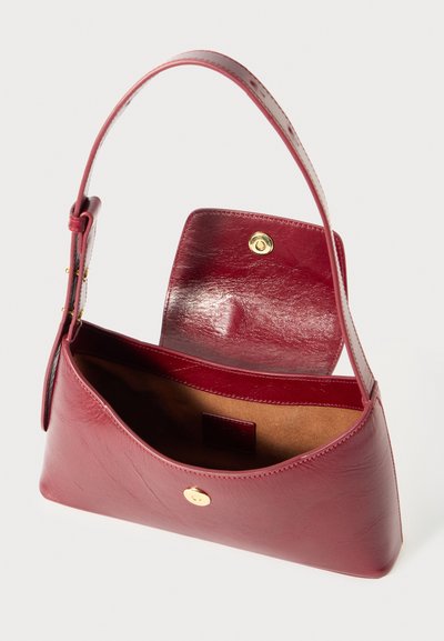 Bolsa de couro vermelho com uma forma curva, uma alça única e um fecho de botão dourado visível. O interior apresenta um forro bege e um bolso.