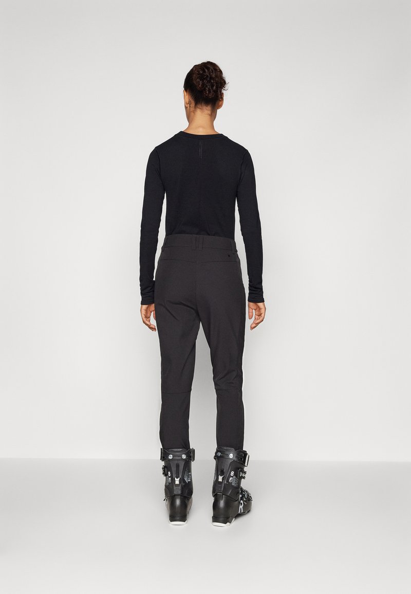 Schwarzes Langarmoberteil kombiniert mit enganliegenden schwarzen Skihosen und schwarzen Skischuhen, mit verstellbarem Bund und elegantem Design.