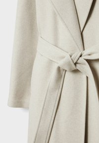 Beżowy wełniany płaszcz o miękkiej fakturze, z kołnierzem typu szal, szerokimi rękawami i materiałowym paskiem wiązanym w talii.