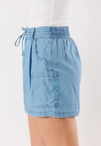 Shorts di jeans azzurri con vita arricciata, dettaglio con laccio e tasca laterale. Il tessuto ha una texture morbida e una vestibilità rilassata.