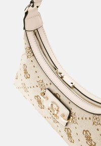 White canvas shoulder bag with gold floral patterns, a contrasting black zipper, and a prominent logo plaque in gold hardware.