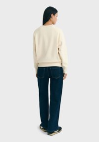 Felpa crema con vestibilità rilassata e polsini a coste, abbinata a jeans denim scuri con design classico a cinque tasche.