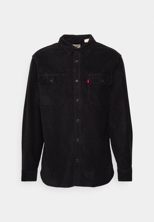 Czarna koszula sztruksowa z długim rękawem, zapinana na guziki z przodu, z dwoma klapkowymi kieszeniami na piersi zapinanymi na guziki oraz małą czerwoną metką na lewej kieszeni.