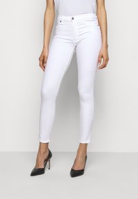 Jeans ajustados blancos de denim, con una cintura de altura media, bolsillos frontales y una textura suave. Combinados con tacones de punta negra.