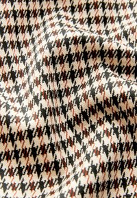 Tkanina w wzór houndstooth z mieszanką czarnego, kremowego i czerwonobrunatnego koloru, o miękkiej, teksturowanej powierzchni.