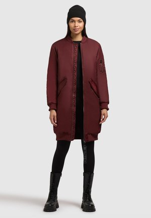Bordeaux kleurige bomberjack met geribbelde manchetten, zijzakken en een opvallende ritssluiting. G gedragen over zwarte leggings en veterschoenen.