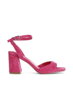 Sandales à talons hauts en suede rose avec un talon carré, bout ouvert et une sangle de cheville ajustable dotée d'une boucle en métal. Texture lisse.