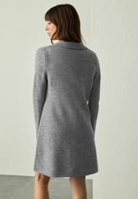 Grå stickad klänning med ribbad krage och långa ärmar. Slät textur, knälång med något utsvängd nederkant. Minimalistisk design.