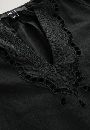 Indumento nero con scollo a V profondo, complessa ricamo in pizzo e dettagli intagliati lungo il collo, realizzato in tessuto leggero.