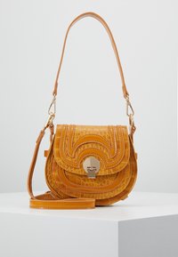 Borsa a tracolla in pelle gialla con texture a coccodrillo, dotata di patta curva e chiusura dorata, esposta su un piedistallo bianco contro uno sfondo semplice.