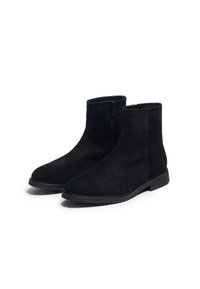 Bottines en daim noir avec une texture lisse, fermeture éclair sur le côté et bout rond. La semelle est plate avec un léger bord surélevé.