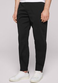 Pantaloni chino neri con una vestibilità su misura, dotati di tasche laterali e realizzati in un morbido tessuto di cotone. Indossati con scarpe da ginnastica bianche e una camicia bianca.