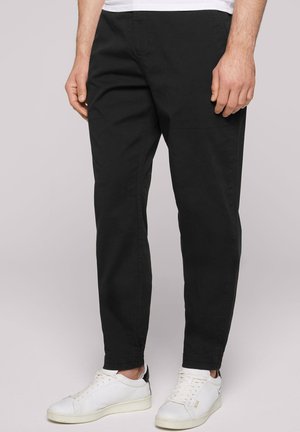 Pantalons chinos noirs avec une coupe ajustée, dotés de poches latérales et d'un tissu en coton lisse. Portés avec des baskets blanches et une chemise blanche.