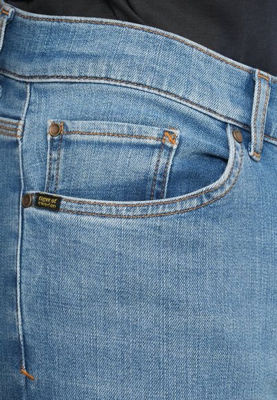 Calças de ganga em azul claro apresentando um design clássico com cinco bolsos, costura laranja e uma pequena etiqueta preta com a inscrição "Tiger of Sweden".