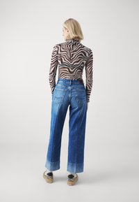 Top de manga larga a rayas marrones y blancas con cuello alto, combinado con unos vaqueros de pierna ancha de mezclilla azul con bolsillos traseros y un dobladillo claro.