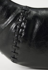Schwarze Kunstledertasche mit strukturiertem Oberflächen und einer dekorativen genähten Detail entlang der Seite mit rechteckigen Aussparungen.