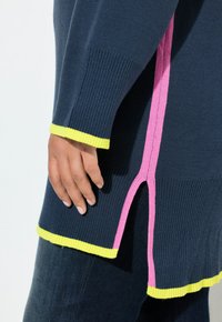 Maglione lavorato a maglia blu navy con texture a coste, accenti laterali rosa e orlo giallo brillante. I dettagli con scollatura laterale migliorano la flessibilità e lo stile.