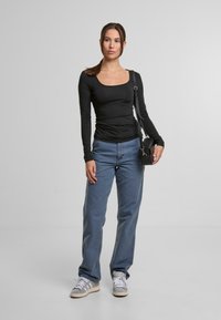 Černý dlouhý rukáv, fitted top, modré volné džíny, šedé a bílé tenisky a malá černá crossbody taška. Jednoduchý design, minimální akcenty.