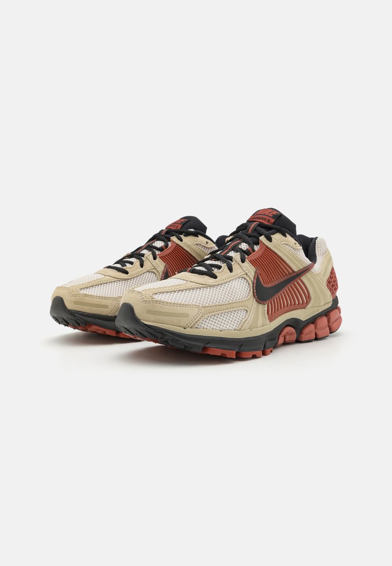 Beżowe i czarne sneakersy z czerwonym akcentem, z siateczkową cholewką, teksturowanymi overlayami oraz amortyzowaną podeszwą z przyczepnym bieżnikiem.