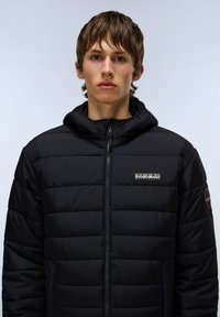 Black puffer jacket with horizontal quilted texture, zippered front, adjustable hood, and logo detail on chest and sleeve.
