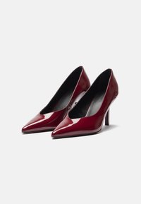 Décolleté in pelle patent bordeaux con punta affusolata, design traforato e tacco alto sottile. Finitura liscia con una texture lucida.